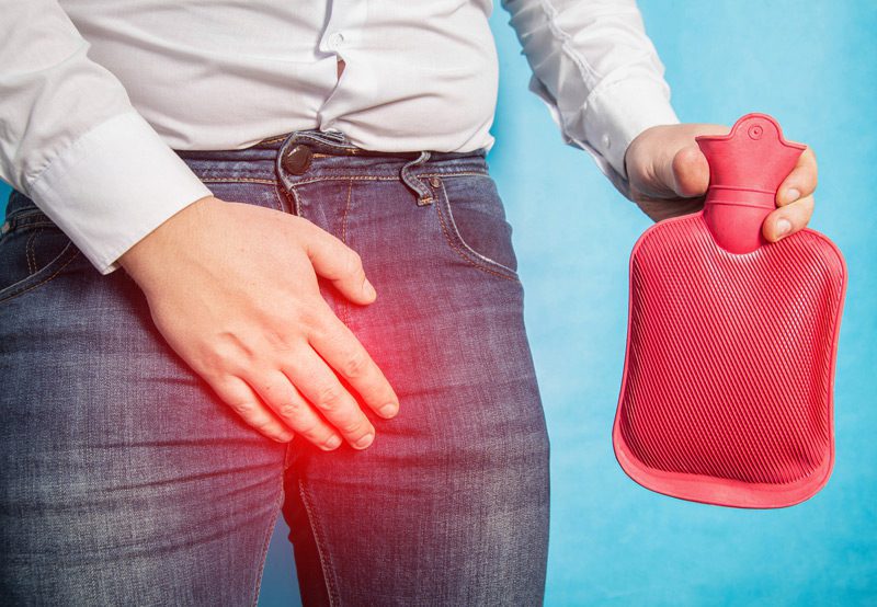 A man holds a red heating pad near his pelvic area